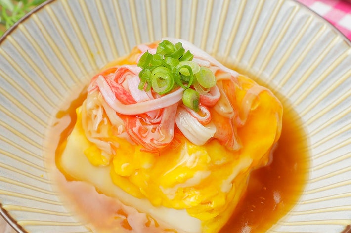 皿の上に出された茶碗蒸し。カニカマとネギでトッピングされ、出汁がかかっている。