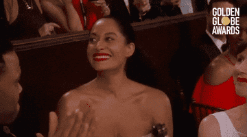 Person in an elegant strapless outfit smiles and claps at a Golden Globe Awards event