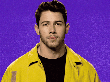 A person with short hair and a trimmed beard wears a casual open jacket over a dark shirt, looking directly at the camera
