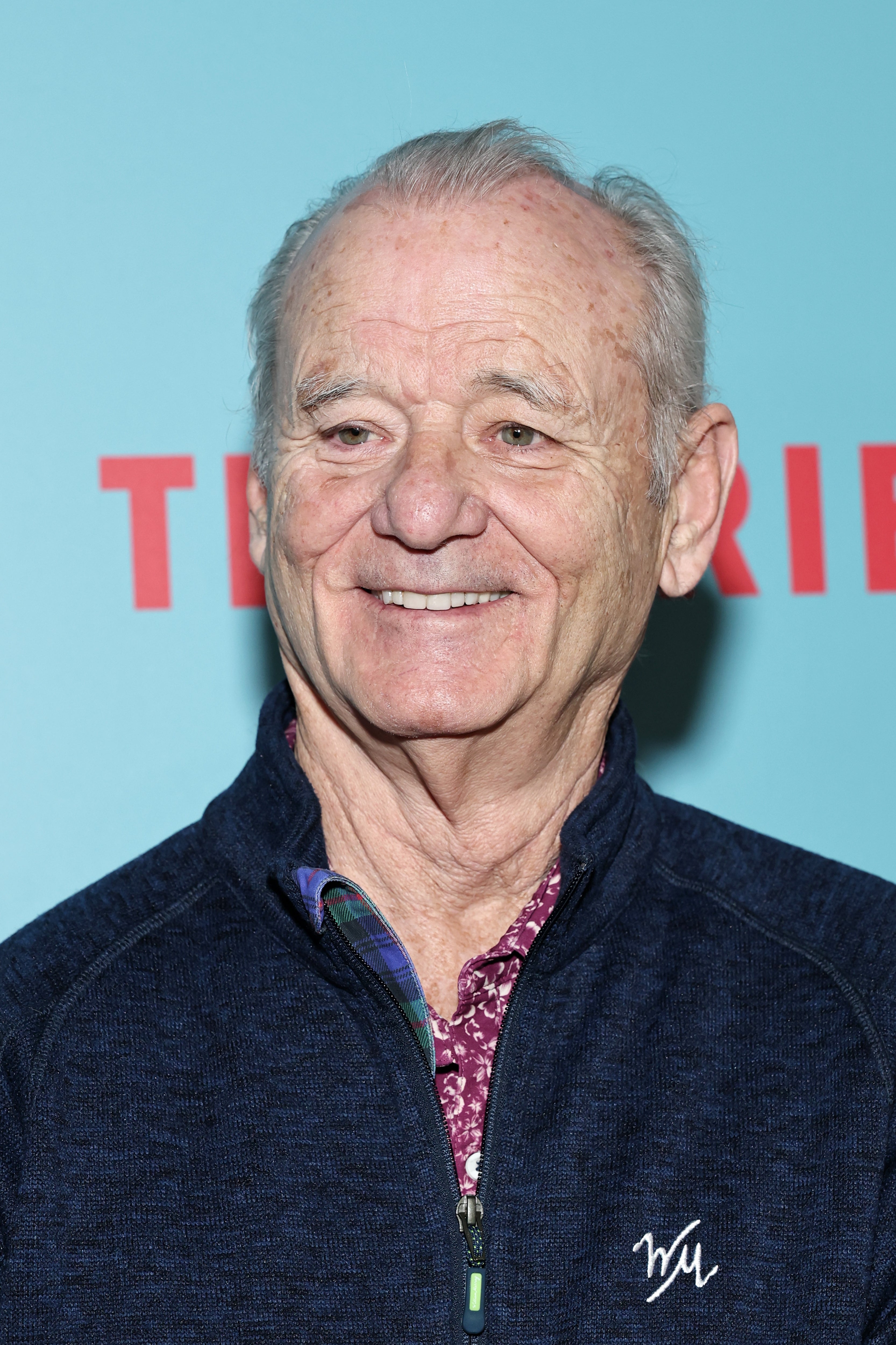 Bill Murray smiling, wearing a casual jacket over a patterned shirt, attending an event