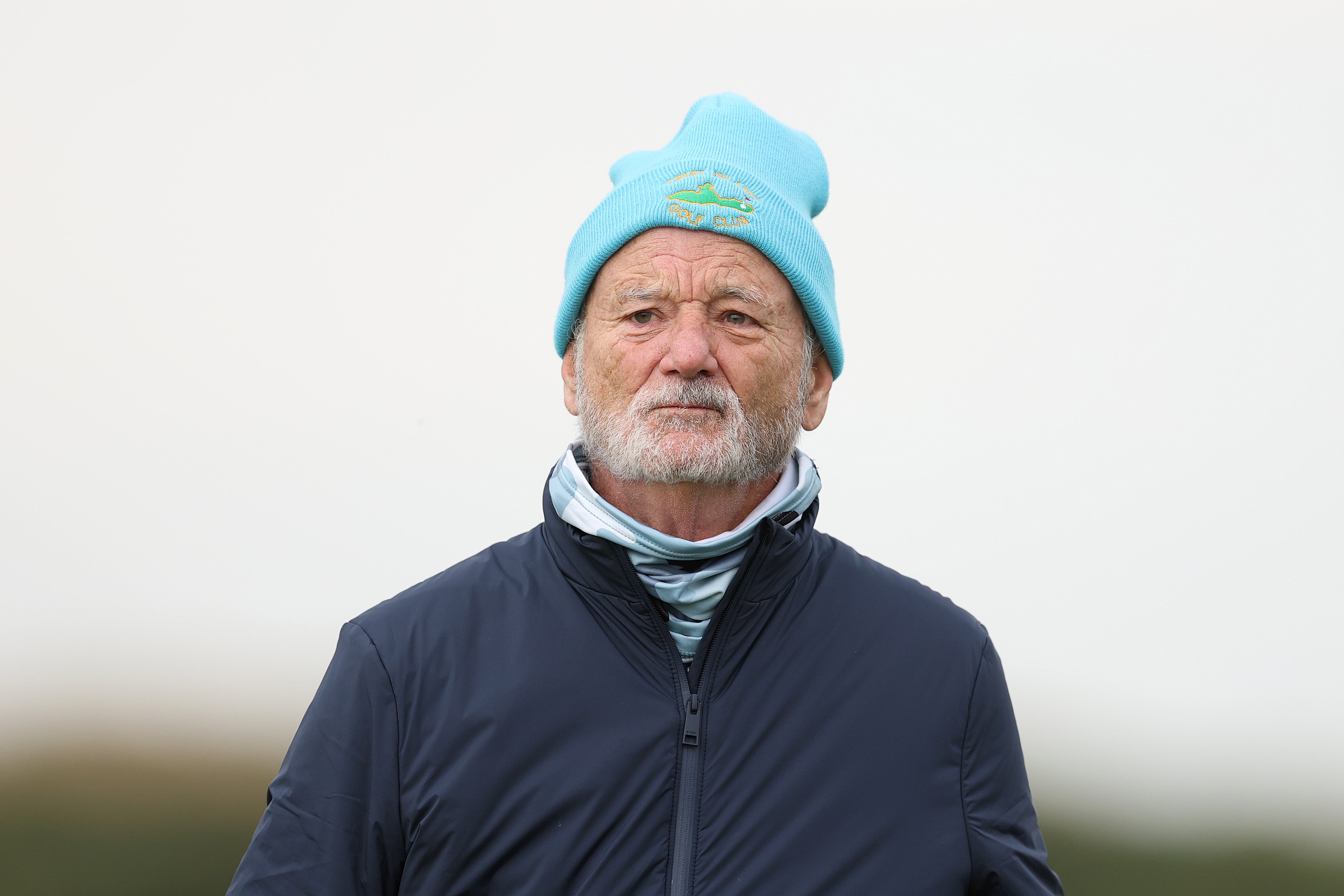 Bill Murray in a blue beanie and dark jacket looks into the distance with a neutral expression