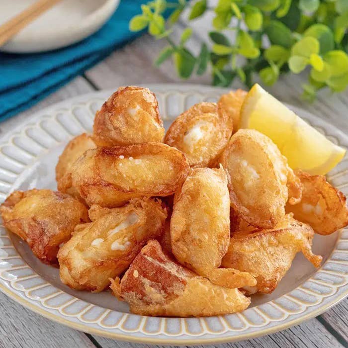 お皿に盛られた揚げたカッテージチーズとレモンのスライス飾り。背景に青い布と箸。