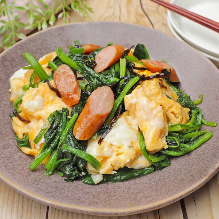 お皿に盛られたほうれん草、スクランブルエッグ、ウインナーの料理。