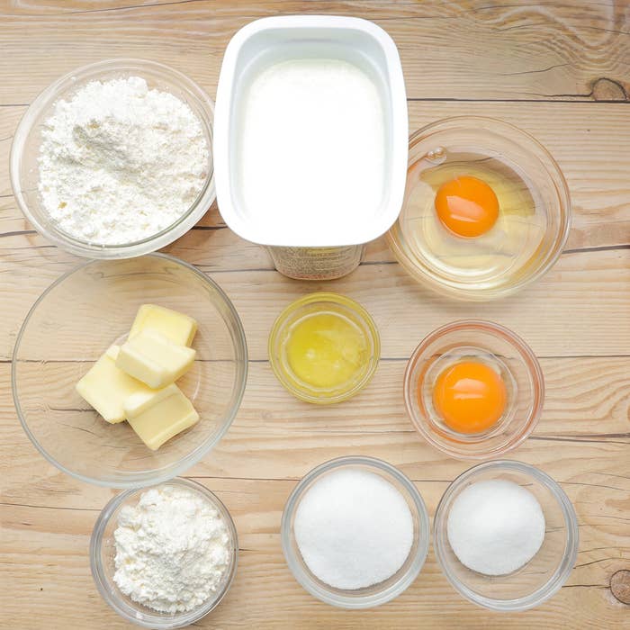 木製テーブルの上に、粉、ヨーグルト、卵、バター、砂糖など材料が並べられています。