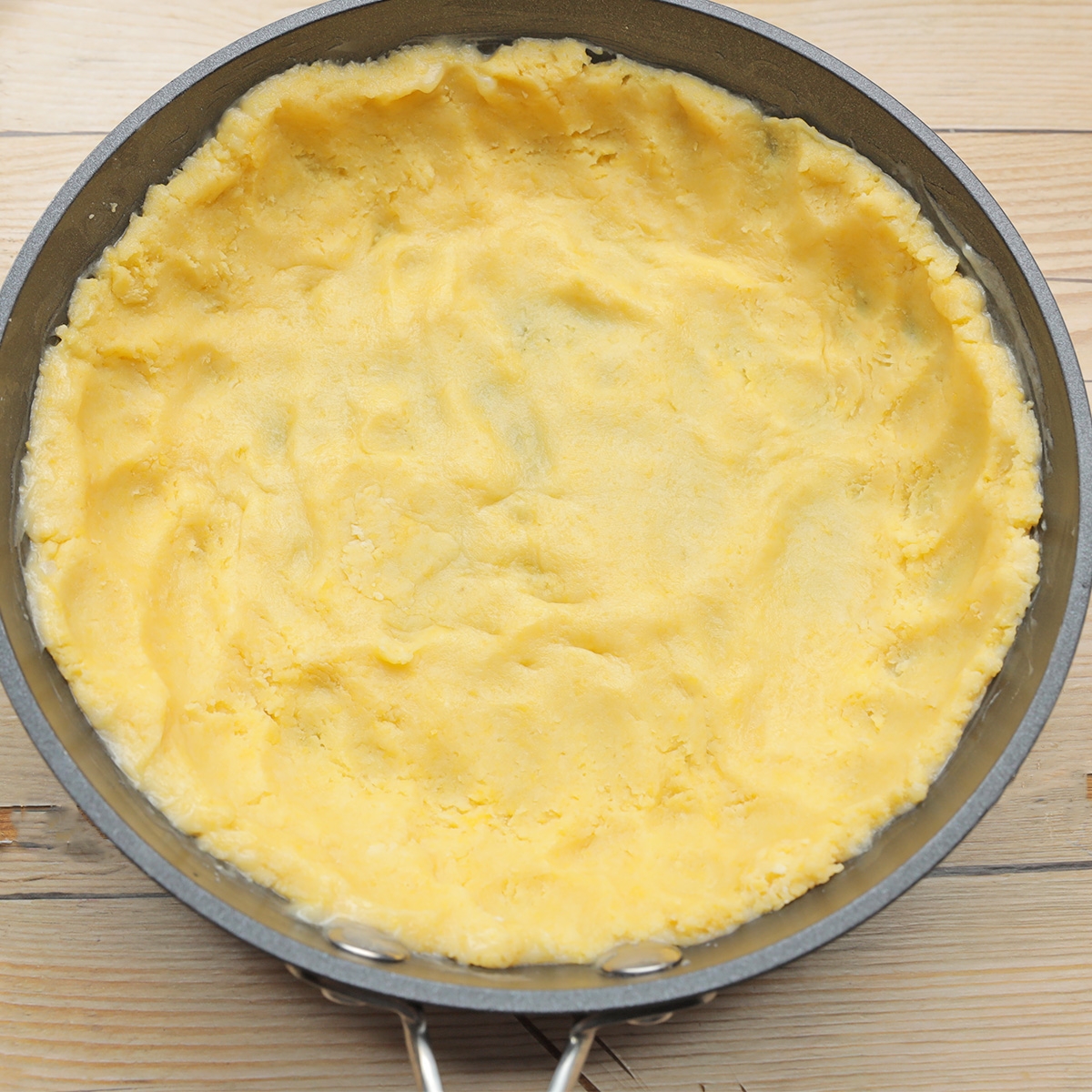 敷き詰められた生地が調理前の状態で、背景には木製の台が見える。