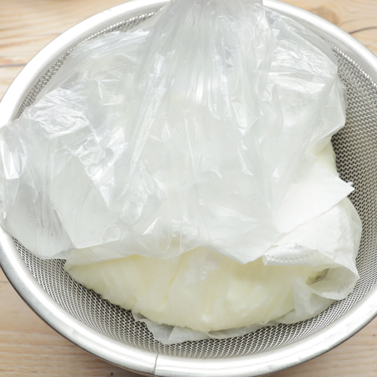 ビニール袋に包まれたヨーグルトが金属製のザルに置かれている様子。