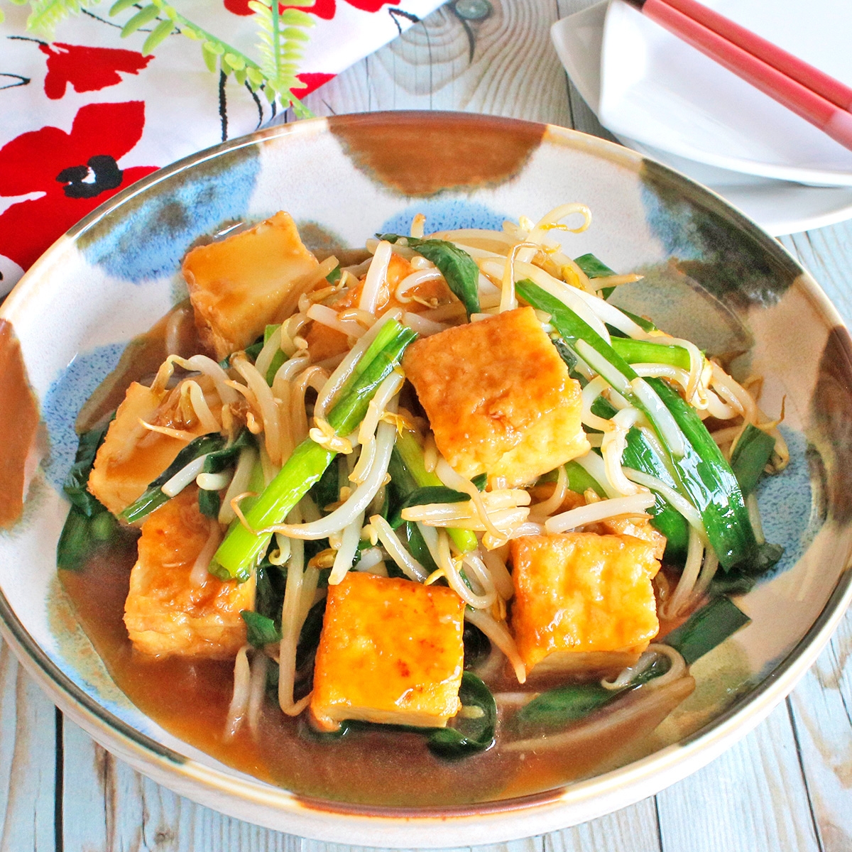 豆腐と野菜の炒め物が盛られた皿。テーブルには割り箸と絵柄入りの布が見える。