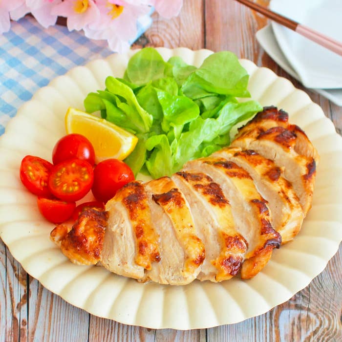 皿に盛られた焼いたチキン、レタス、ミニトマト、レモンスライスがあり、食卓にセットされています。