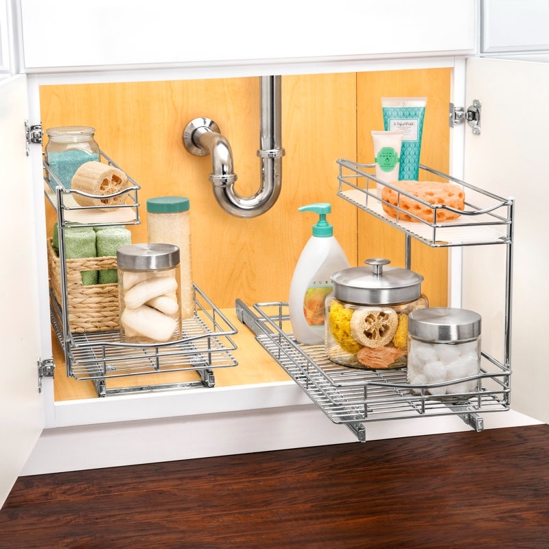 Organized under-sink cabinet with sliding metal racks holding various cleaning and personal care items in jars and bottles