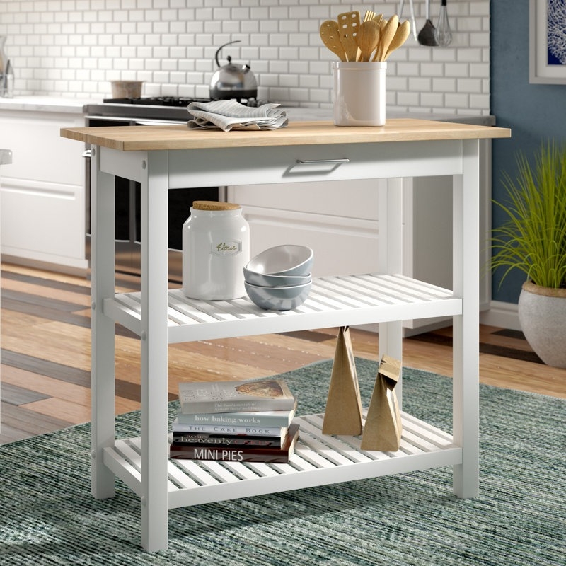 Kitchen island with wooden top, two shelves holding kitchenware and books, located in a modern kitchen with sleek cabinetry and backsplash