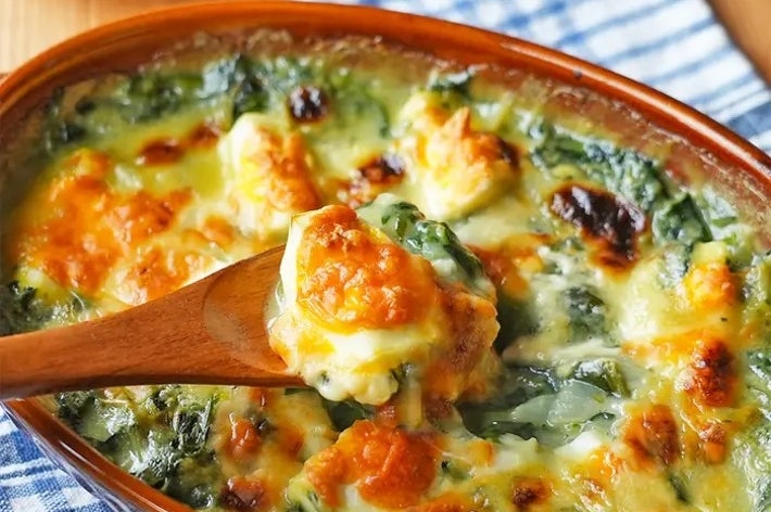 オーブン焼きのチーズと野菜が入ったグラタン、木製スプーンですくわれた一部が見えます。