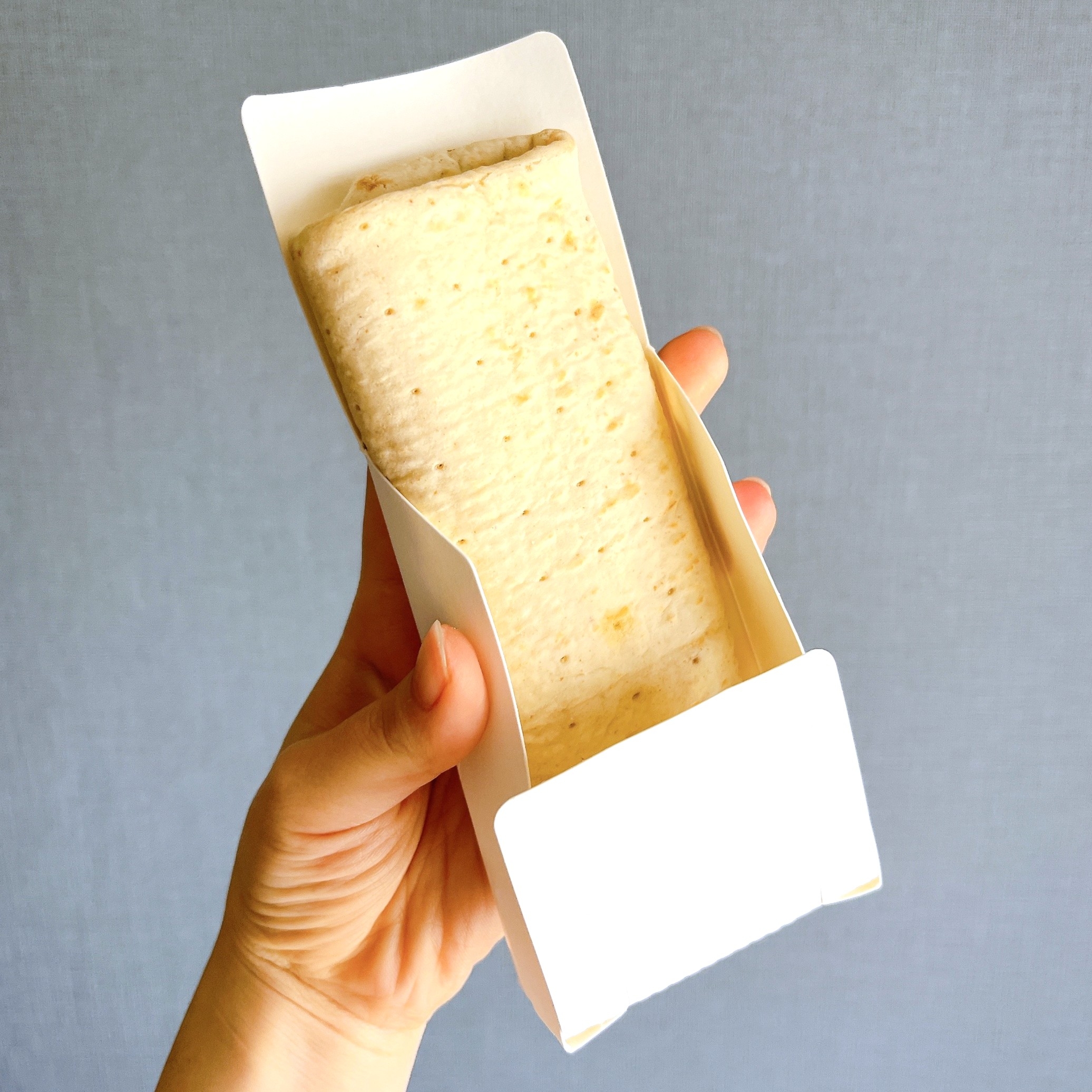 手に持たれたチーズ味のアイスサンドイッチ。紙トレイに包まれています。