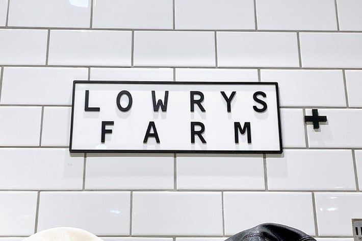 白いタイル壁の上に「LOWRYS FARM」と書かれた黒い文字の看板が掲示されています。