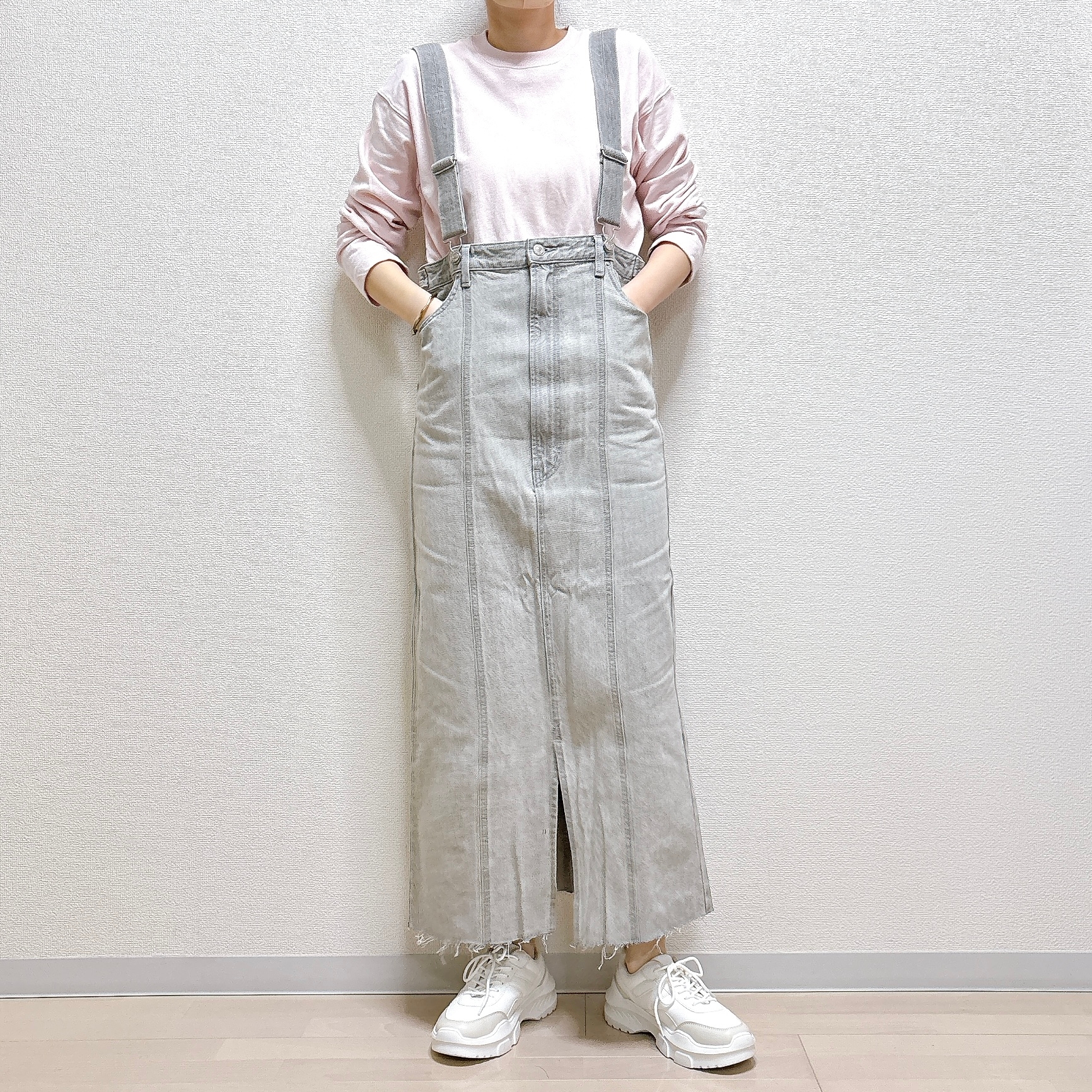 白いスニーカーを履き、カジュアルなデニムのオーバーオールスカートを着た人が立っています。