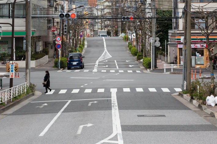 交差点で横断歩道を渡る歩行者と停車中の車。静かな街の風景。