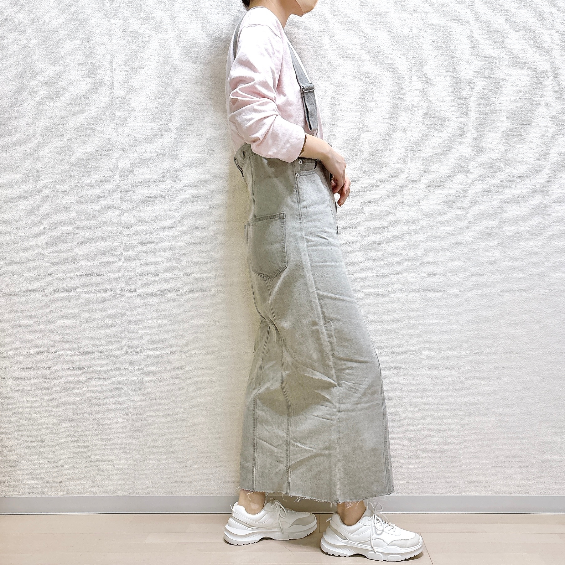 横向きに立つ人が、カジュアルなオーバーオールとスニーカーを着用しています。