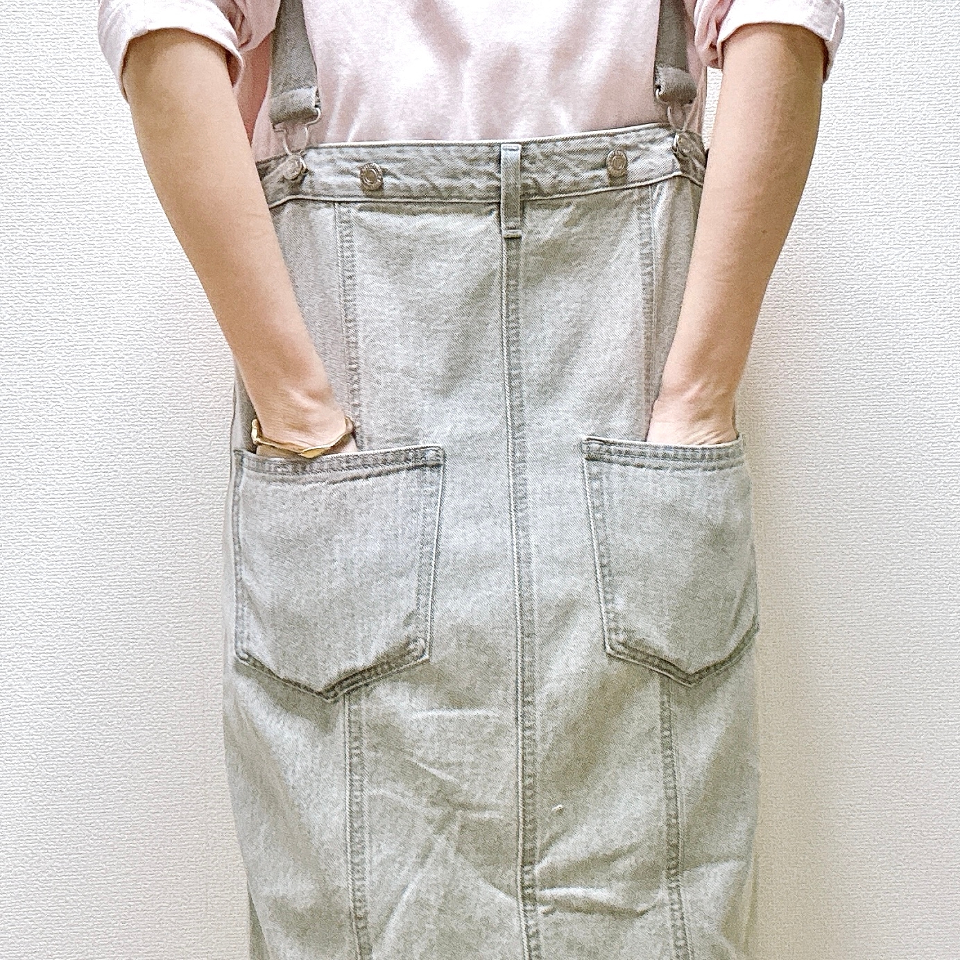 人がサスペンダー付きのデニムスカートを着用し、後ろ姿でポケットに手を入れている様子。