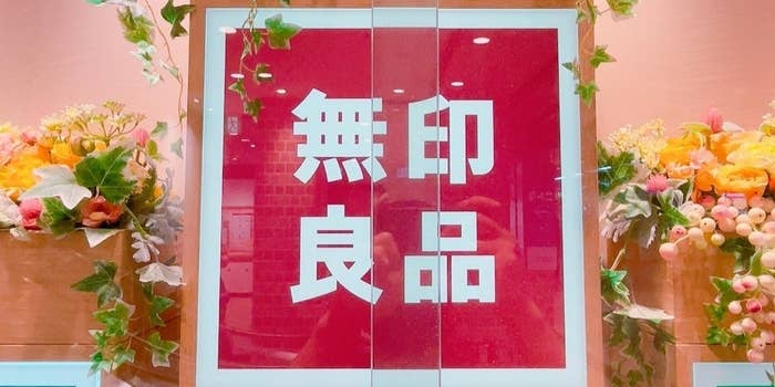 背景に花が飾られた「無印良品」の看板。