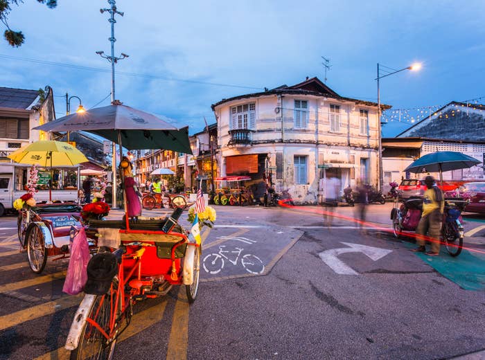 Bustling street scene with rickshaws parked near vibrant shops and a colonial-style building in the background, capturing dynamic urban life