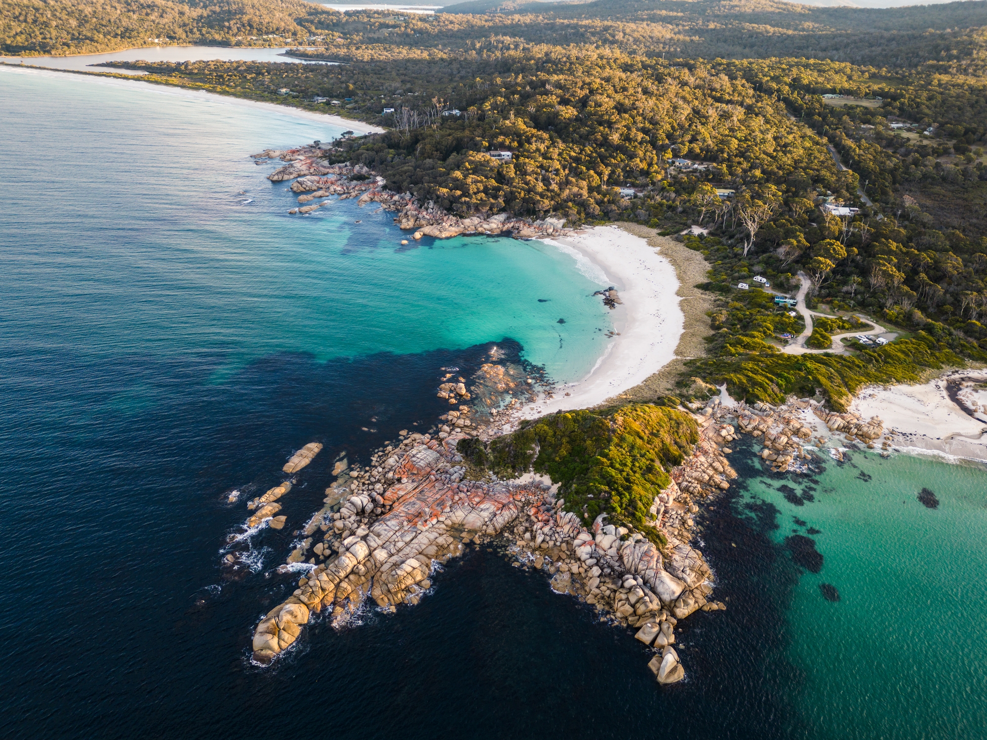 Aerial view of a scenic coastline with rocky outcrops, sandy beaches, and lush greenery meeting the ocean