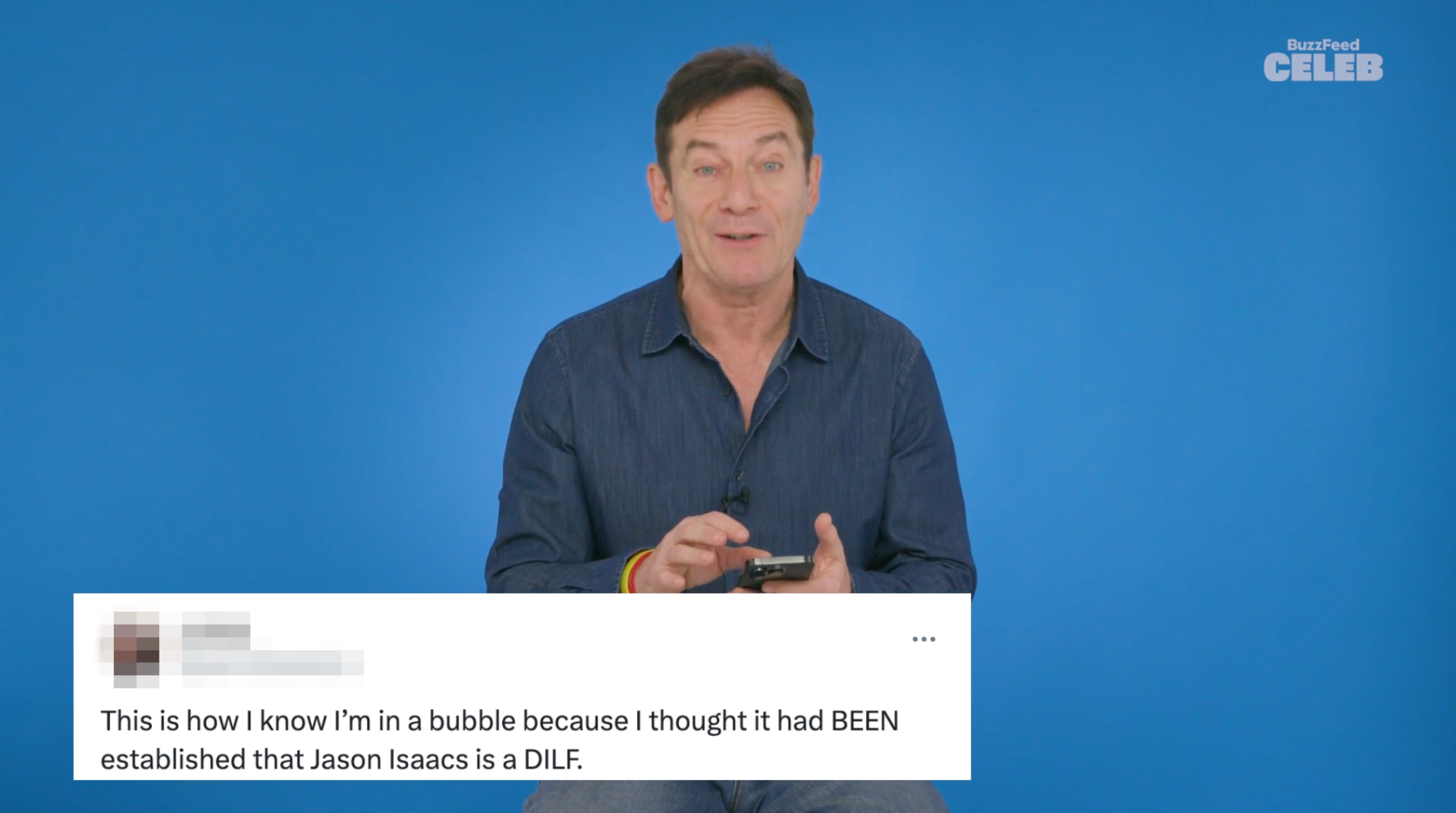 A person in a casual shirt is reading a humorous social media comment about being surprised that Jason Isaacs is considered a DILF