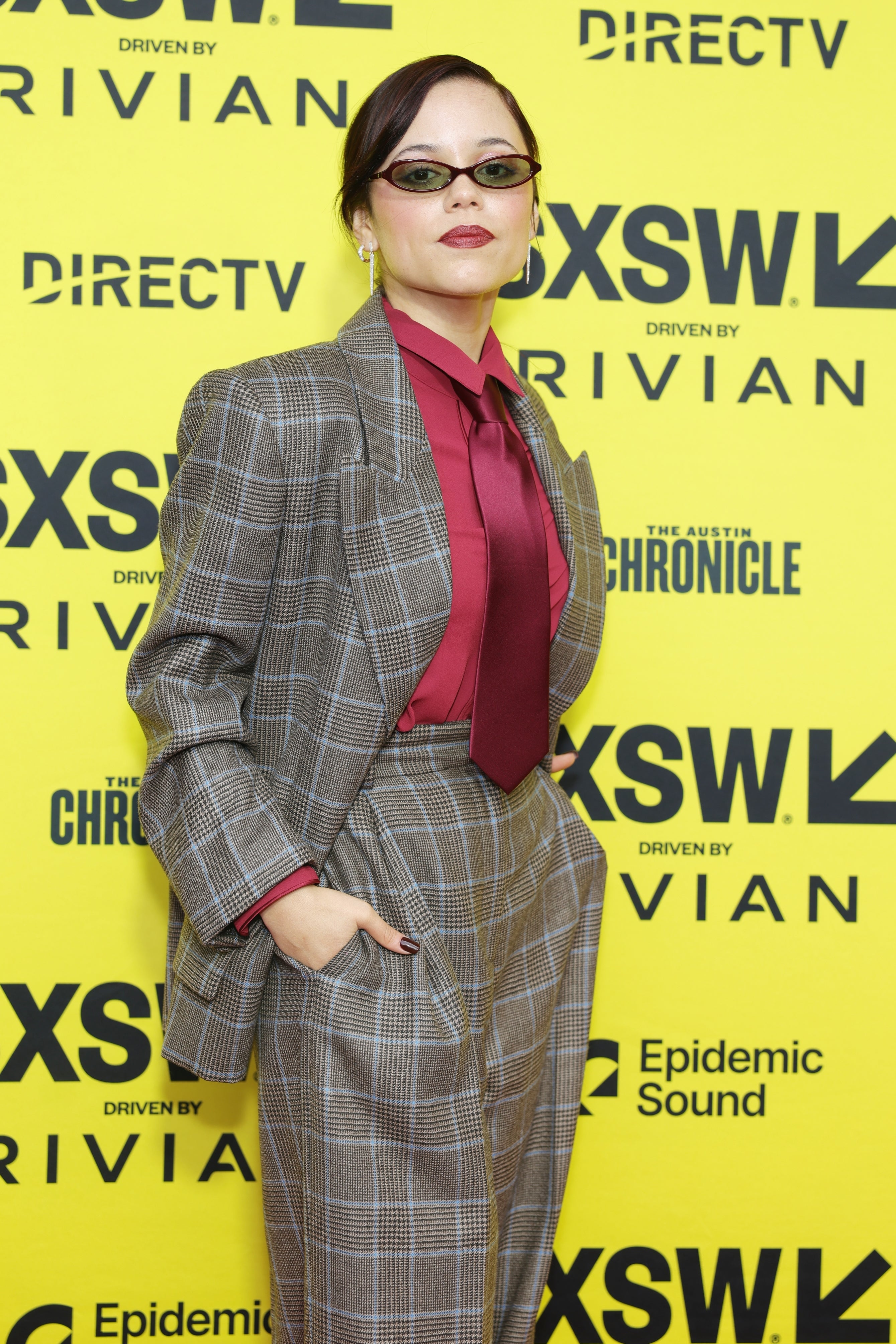 Jenna Ortega in a plaid suit and red shirt at a SXSW event, posing confidently