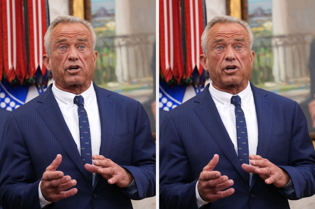 A person in a pinstripe suit speaks with hand gestures in a formal setting, featuring a decorative backdrop and framed picture