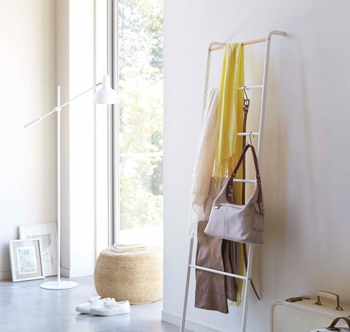 Modern room with a white standing lamp, a ladder holding scarves and a bag, and decor items, suggesting stylish organization and minimalism