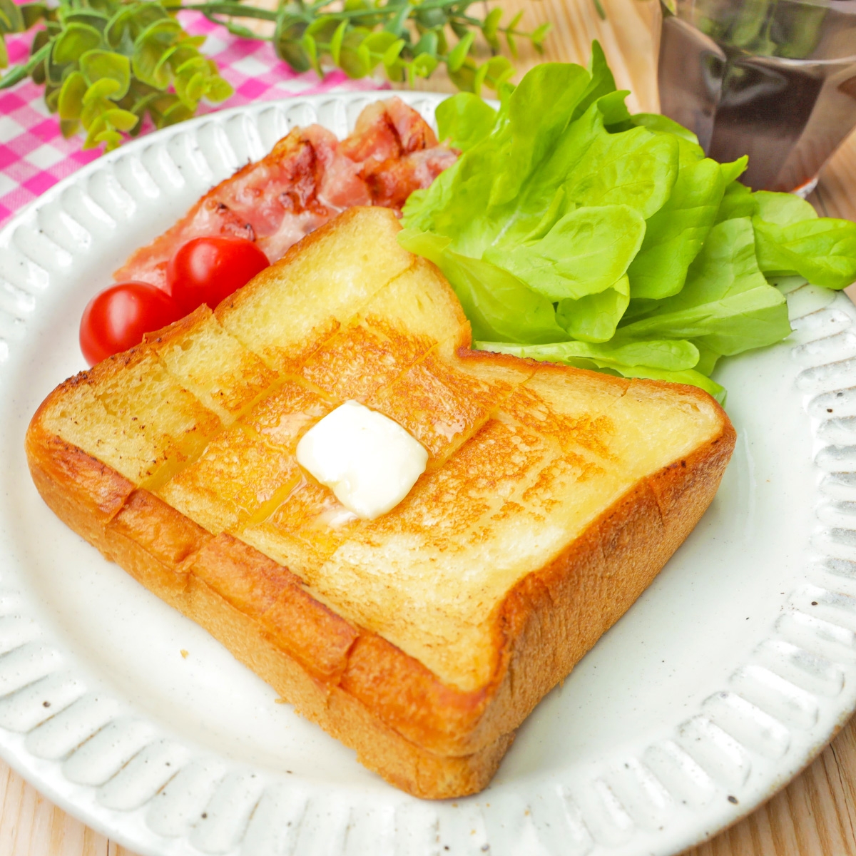 トーストにバター、レタス、ベーコン、ミニトマトが並ぶプレート。朝食にぴったりな美味しそうな盛り付け。