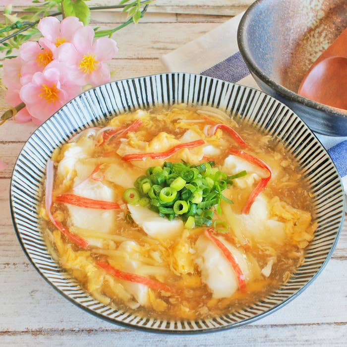 器に盛られた中華スープ。カニカマと刻んだネギがトッピングされ、花が添えられている。