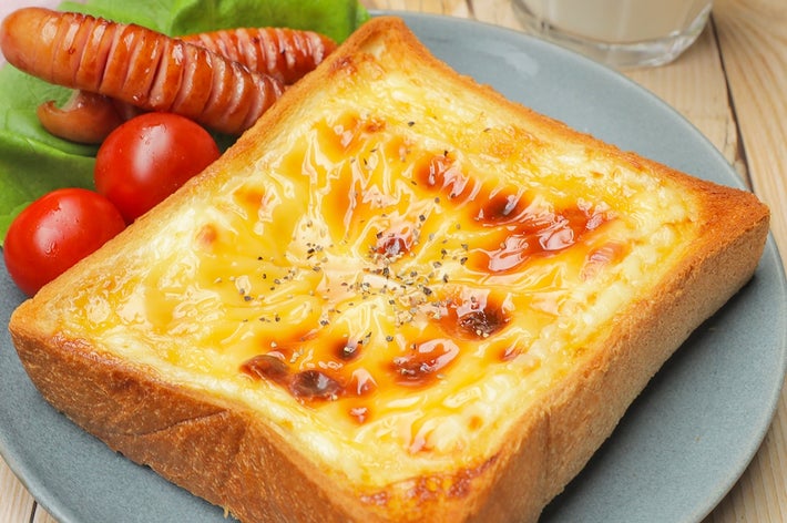 トーストに溶けたチーズとソースをかけた朝食プレート。ソーセージとトマト、ミルクが添えられている。