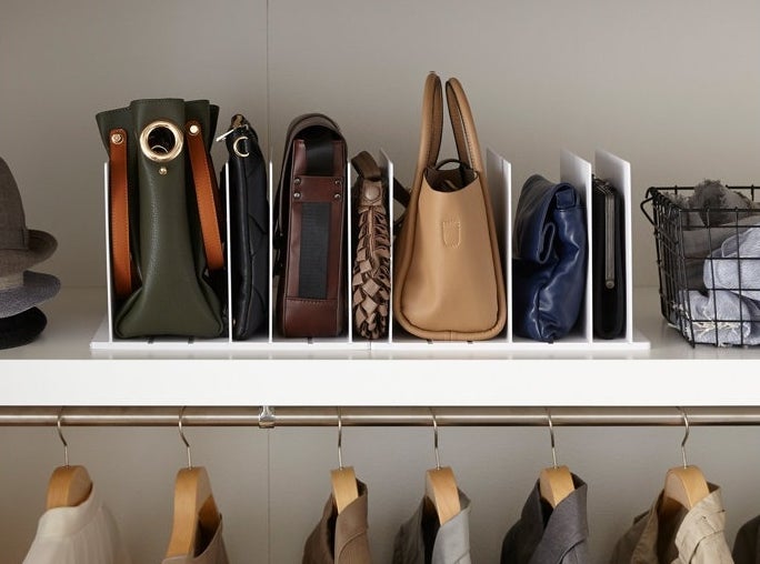 Closet shelf with organized assorted handbags in dividers, hats to the side, and shirts hanging below. Text: &quot;Store an assortment of bags even in a closet with limited space.&quot;