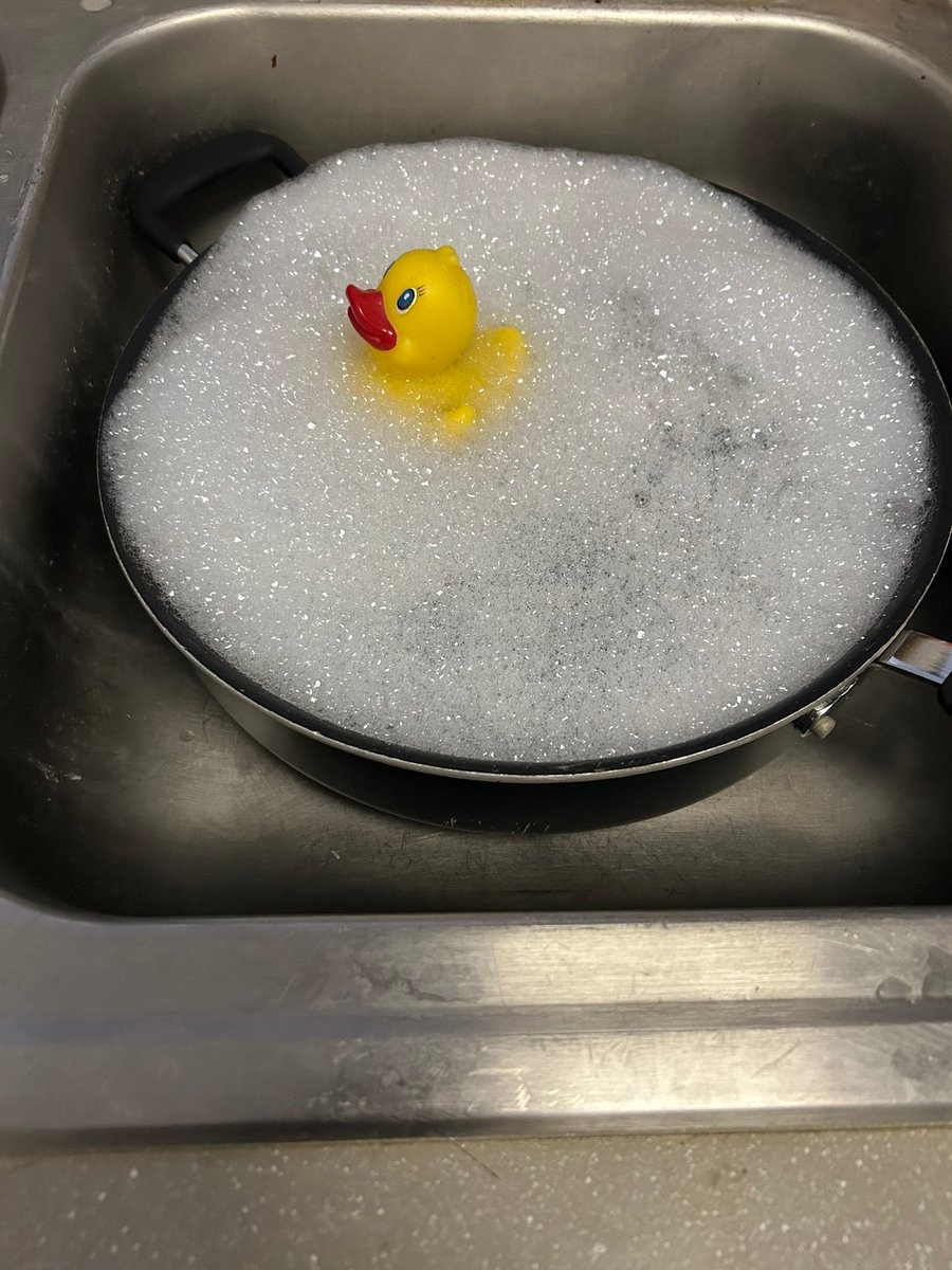 A rubber duck floats amidst bubbles in a soapy pan placed in a kitchen sink