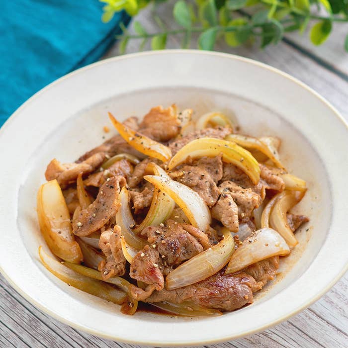 玉ねぎと一緒に炒めた豚肉料理が白い皿に盛られている。シンプルなテーブルでの撮影。