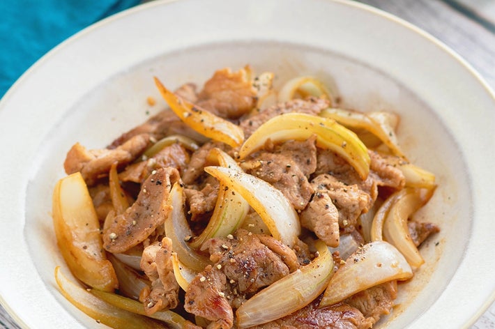 皿に盛られた炒めた肉とタマネギの料理。背景に緑の植物。