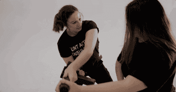 Two women in self-defense training practice disarming techniques with a fake weapon