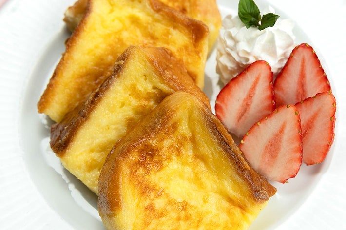 フレンチトーストが皿に並び、横にホイップクリームとスライスされたイチゴが添えられています。
