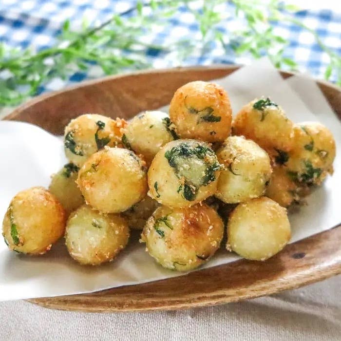 揚げたジャガイモボールが木の皿に盛られている。パセリがトッピングされている。