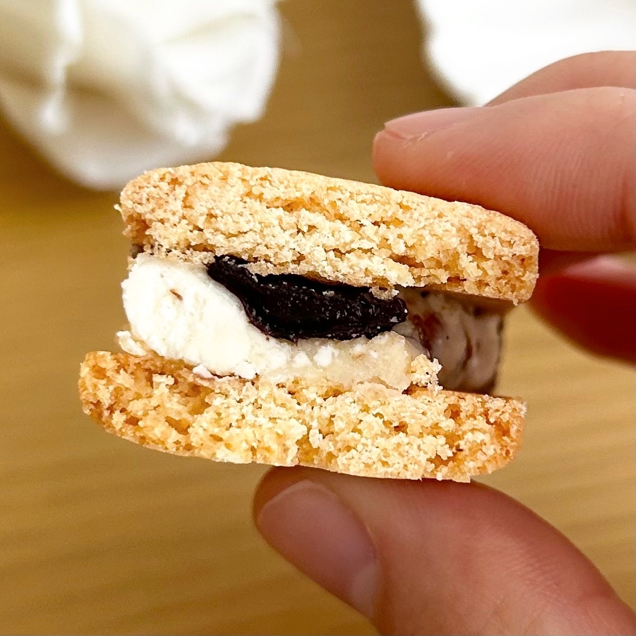 手で持たれたクッキーサンド。中にはクリームとチョコレートが挟まれている。