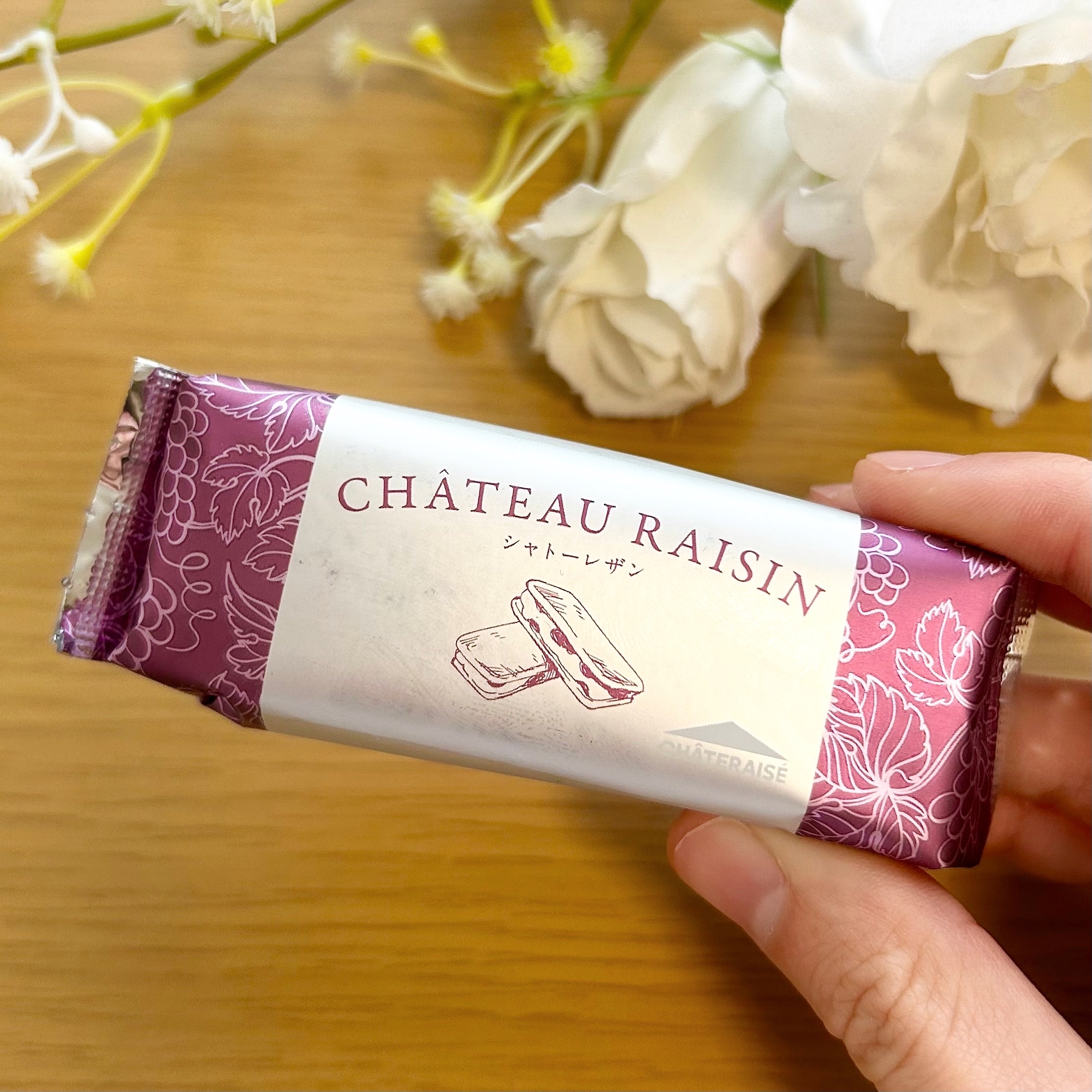 白い花の横に置かれた「シャトーレザン」と書かれたお菓子のパッケージを手で持っている。
