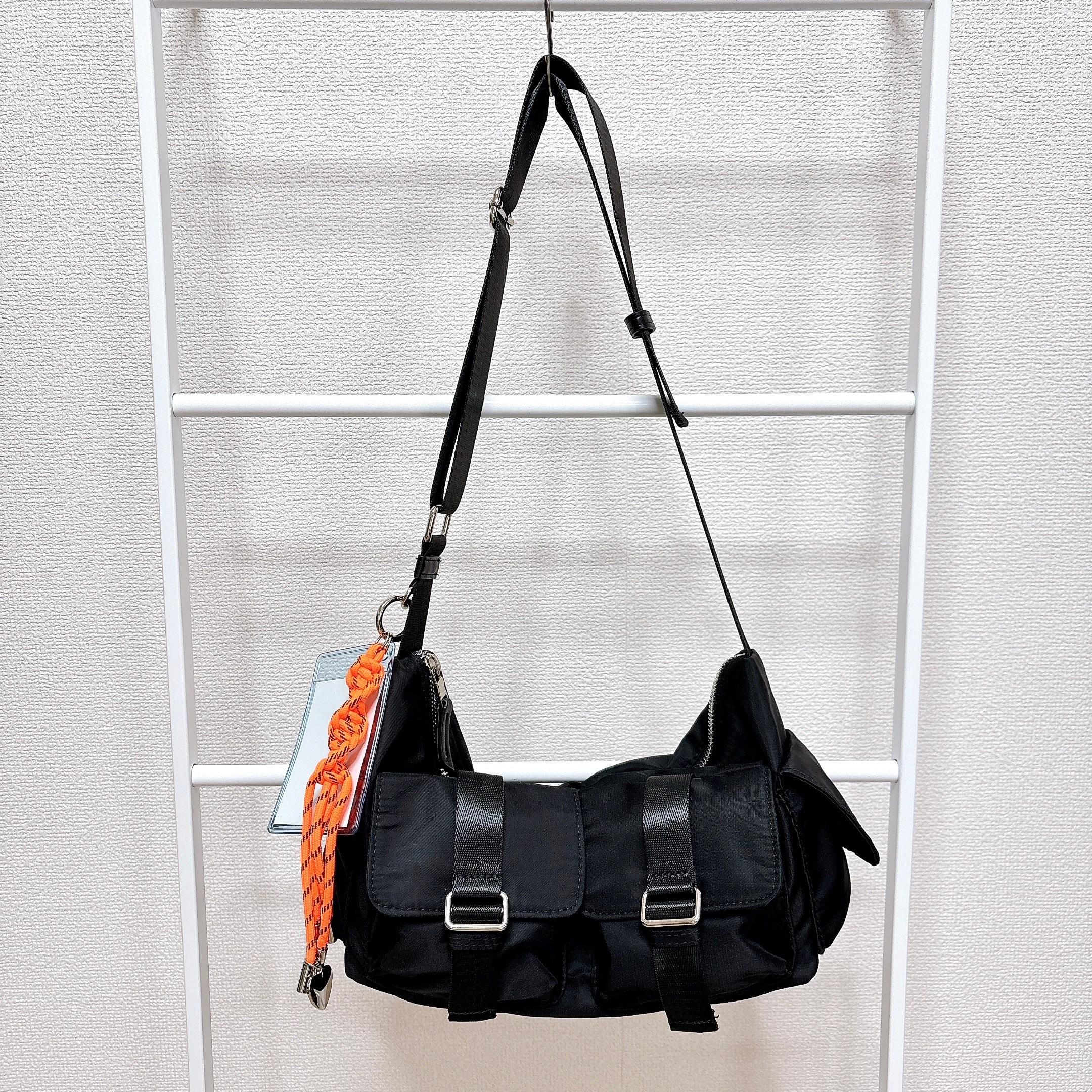 黒いショルダーバッグが白いラックに掛かっている。オレンジのアクセサリーが付いている。