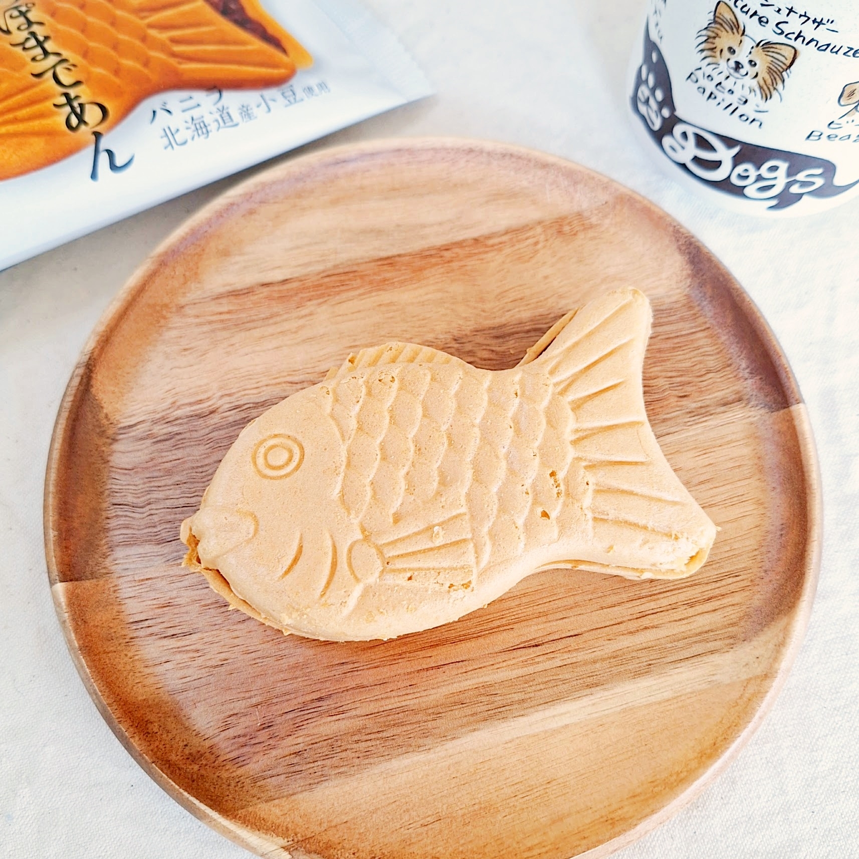 魚型のたい焼きが木製の皿にのっており、背景にはカップと包装。