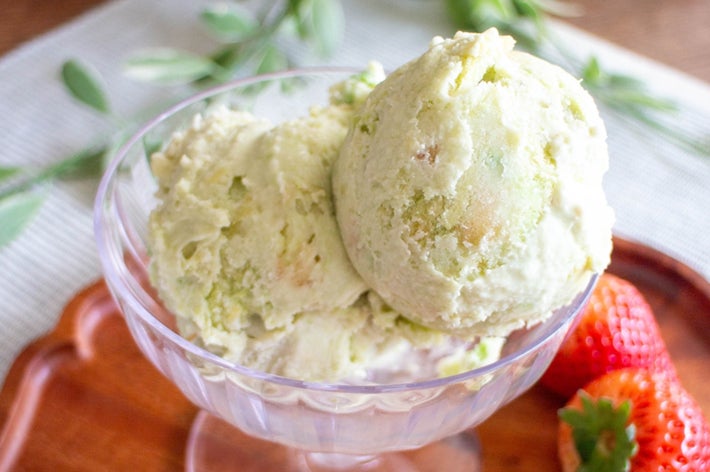 ガラスの器に入ったクリーミーなアイスクリーム2スクープと、横に添えられた2つのイチゴ。スプーンが側に置かれている。