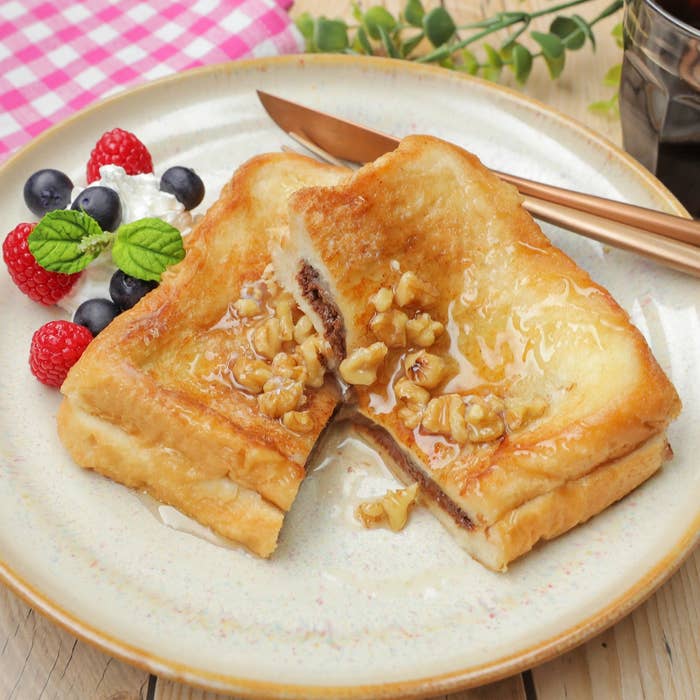 ハチミツとクルミがのったトーストが皿に盛られている。周りにラズベリー、ブルーベリー、ホイップクリームが添えられている。