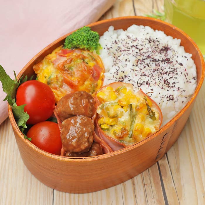 弁当箱にご飯と紫蘇、ミートボール、プチトマト、ブロッコリー、卵料理が入っている。