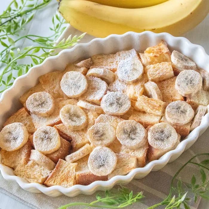 バナナとパンをオーブンで焼いたデザートが白い皿に盛られている。皿の周りにバナナと緑の装飾がある。