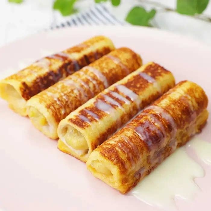 3本のクレープ状のパンケーキがピンクの皿に並び、甘いシロップがかかっています。