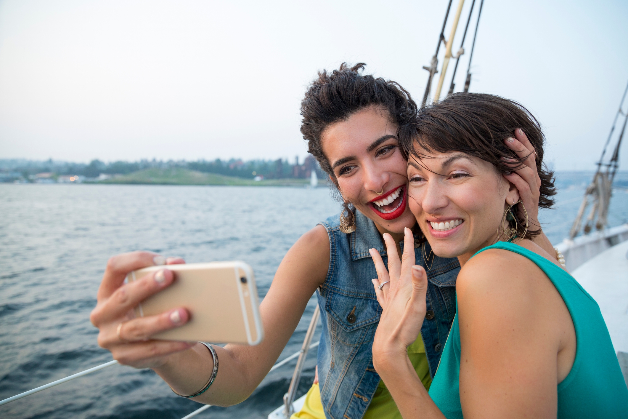 Two people smiling and taking a selfie on a boat with water and land in the background