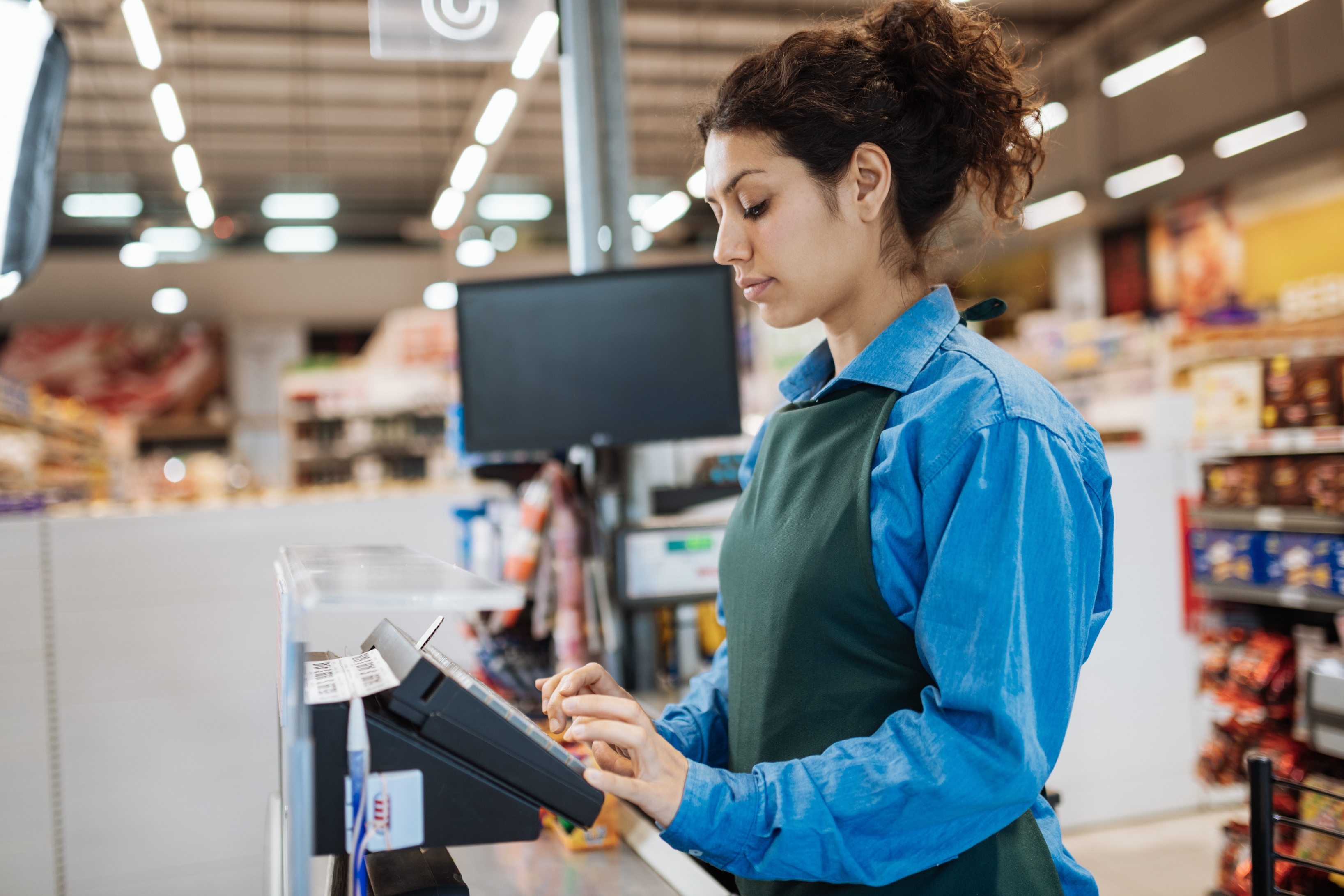 Retail employee at a checkout counter using the touchscreen register, focused and working in a grocery store setting