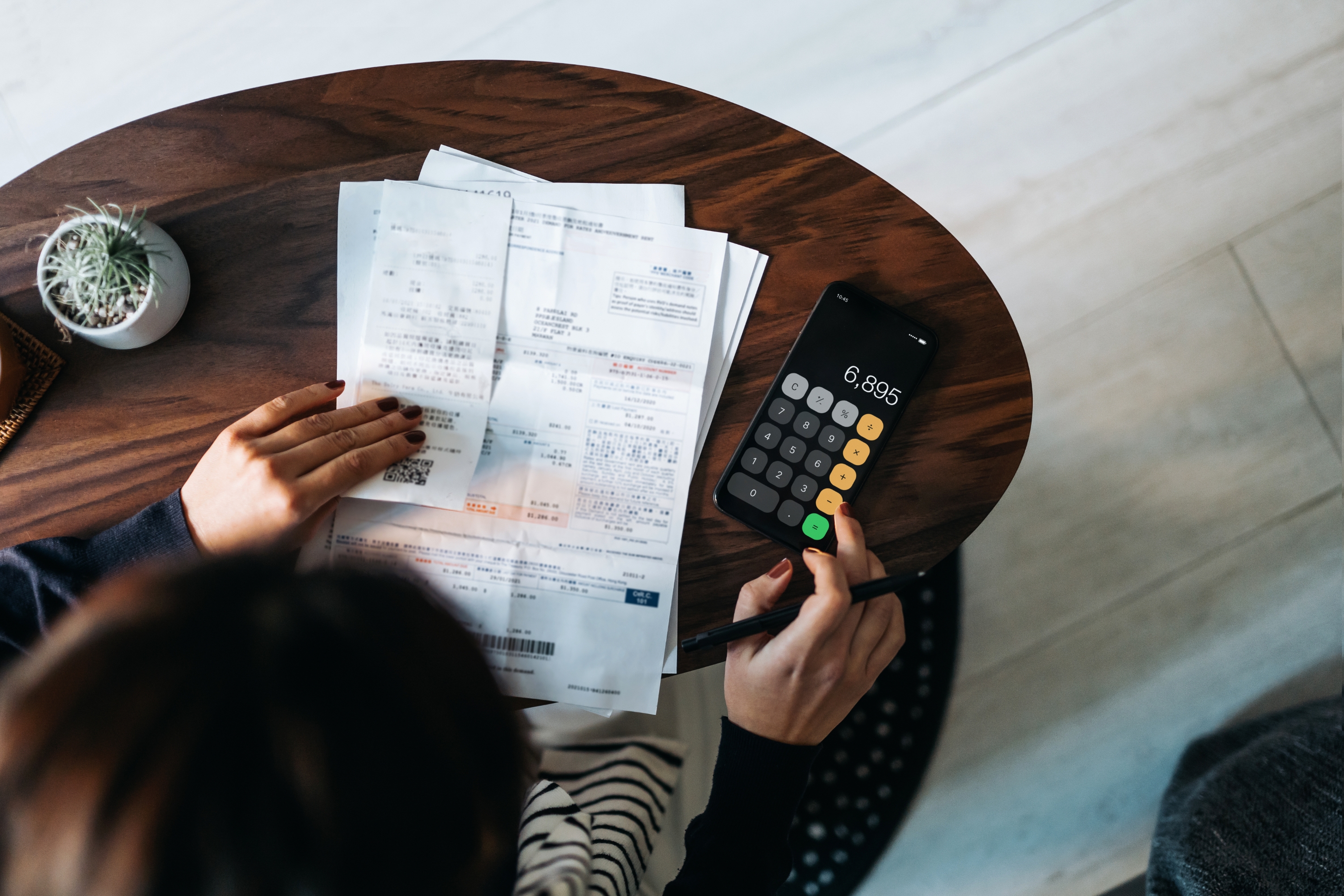 Person using a calculator at a table, surrounded by various bills and receipts, suggesting financial management or budgeting activity